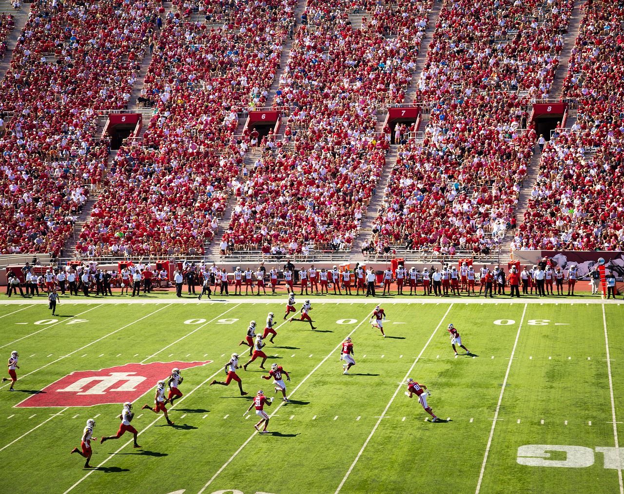 Luchtfoto van een drukbezochte college football wedstrijd bij Indiana University, met spelers in actie op het veld en fans op de tribunes.