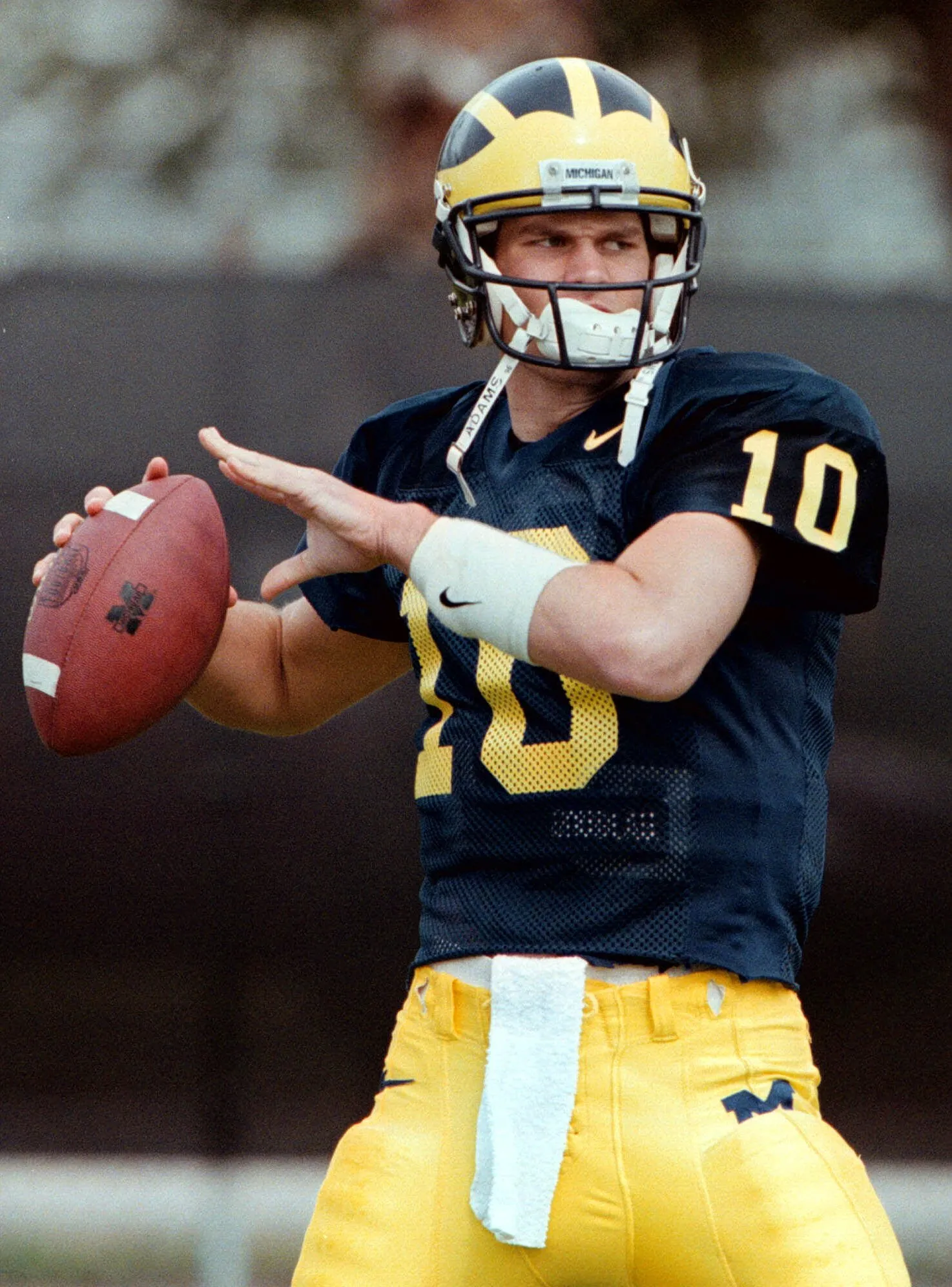 Jonge Tom Brady in actie als quarterback voor de University of Michigan tijdens een college football wedstrijd, gekleed in het blauw-gele tenue van het team.